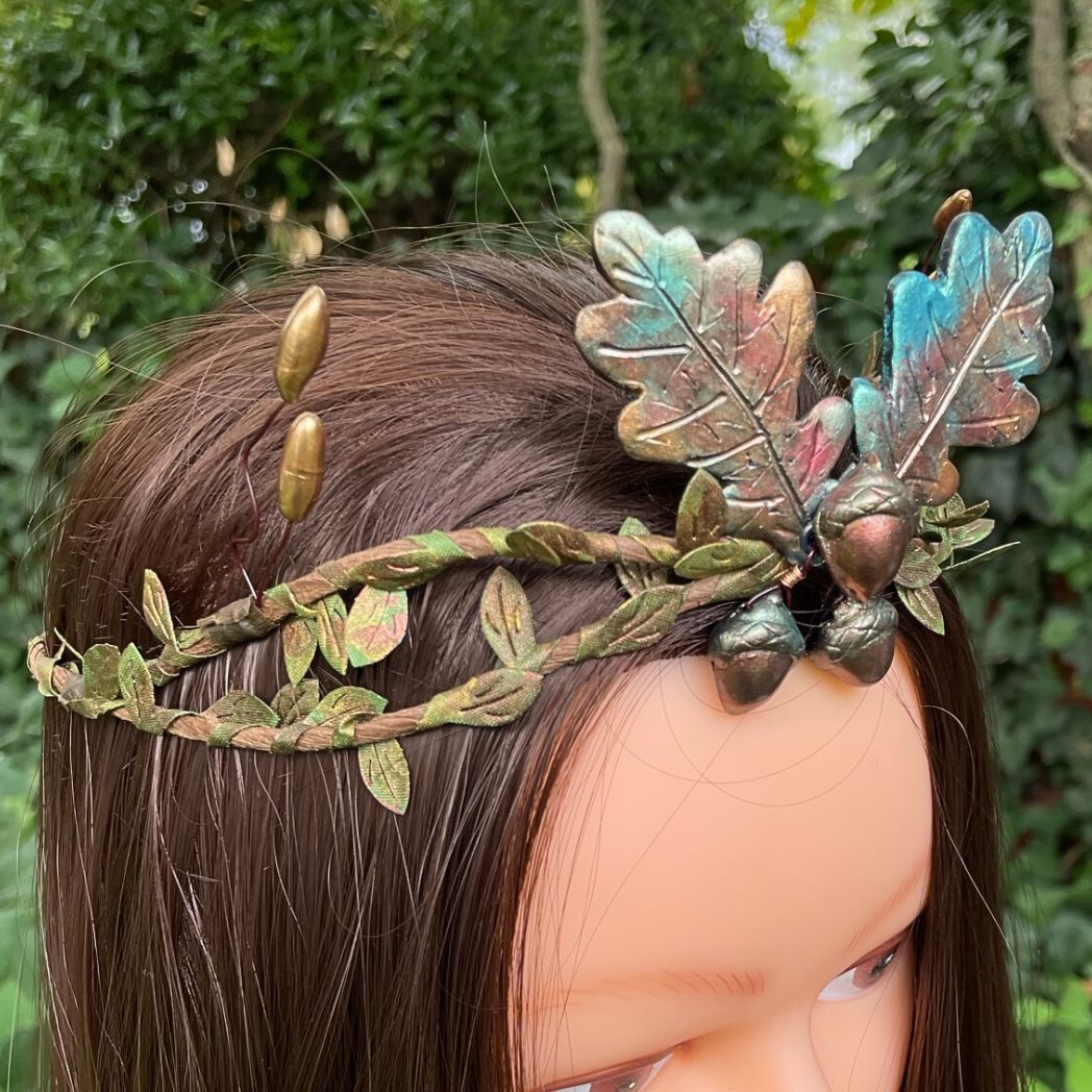 side profile of 3 Acorns and 2 oak leaf crown in muted Fall colors with green and gold leaf vines and golden buds to the sides.  The crown is displayed on a model
