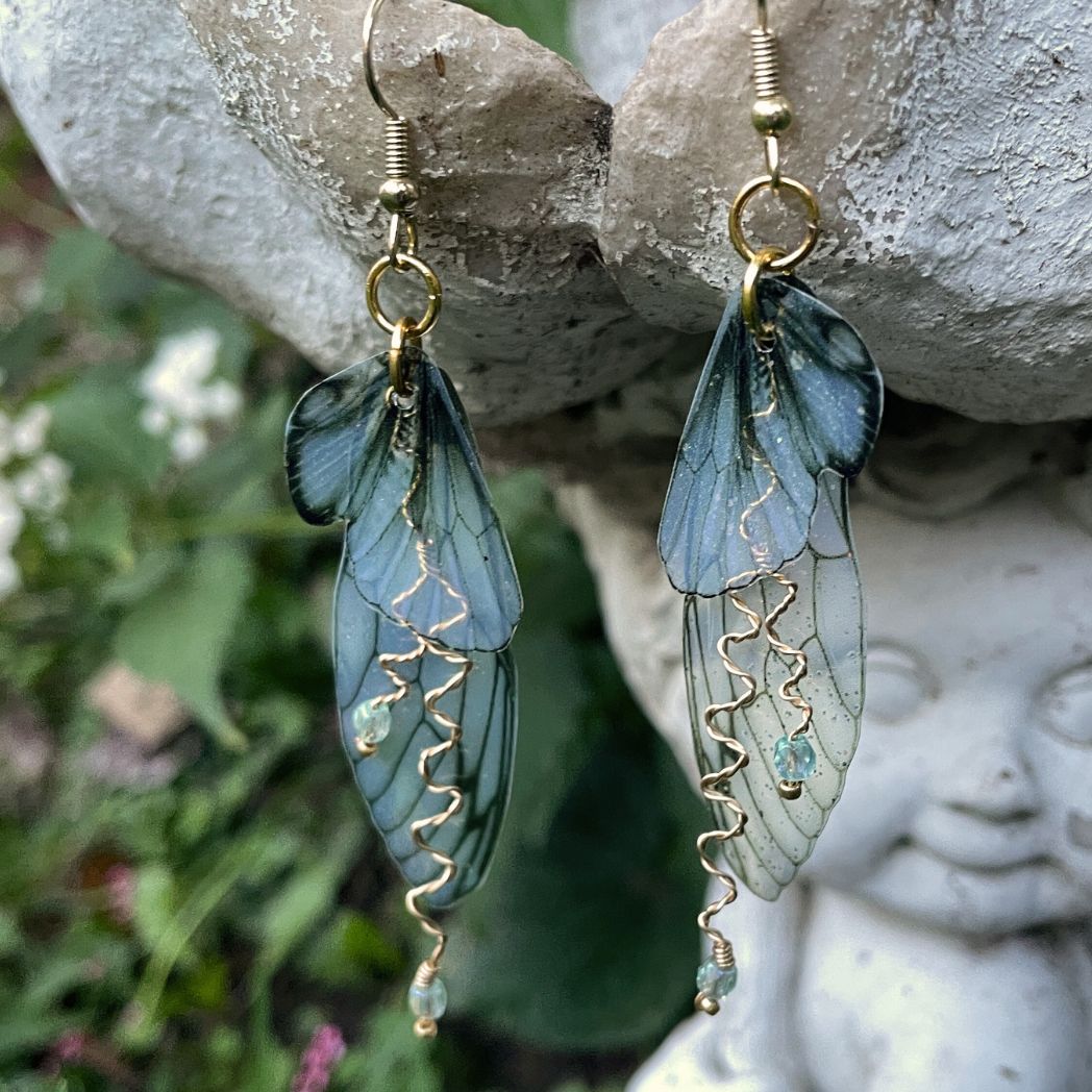 olive green fairy earrings suspended on a garden ornament in a garden setting.