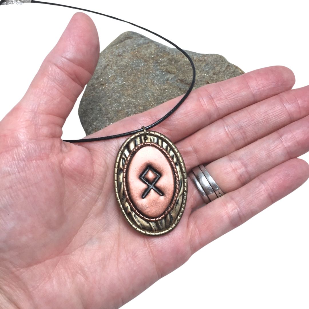 Othala rune pendant necklace held in a hand on white background with a rock in the background
