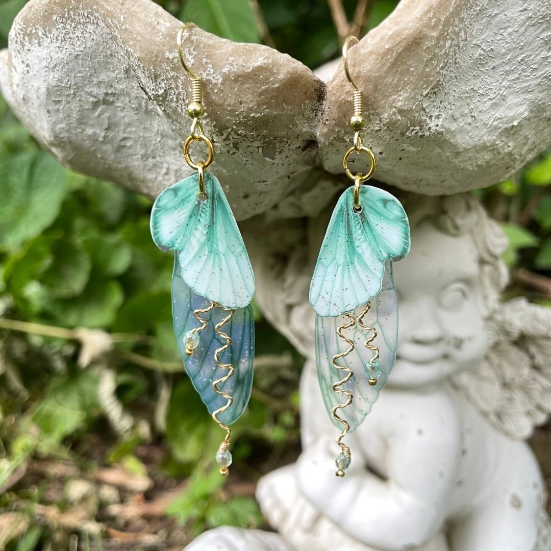 Mint green double wing fairy wings with gold twisted wires with crystals. and gold french ear hooks hanging on a angel garden ornament.