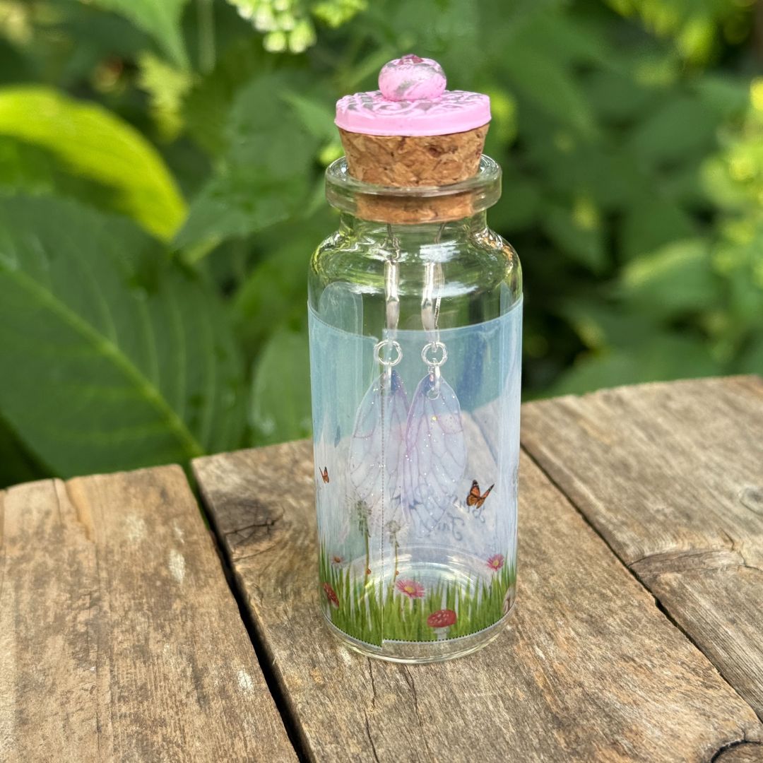 Decorative bottle with a cork lid, fairy house, and butterfly on a wooden surface with green foliage in the background.