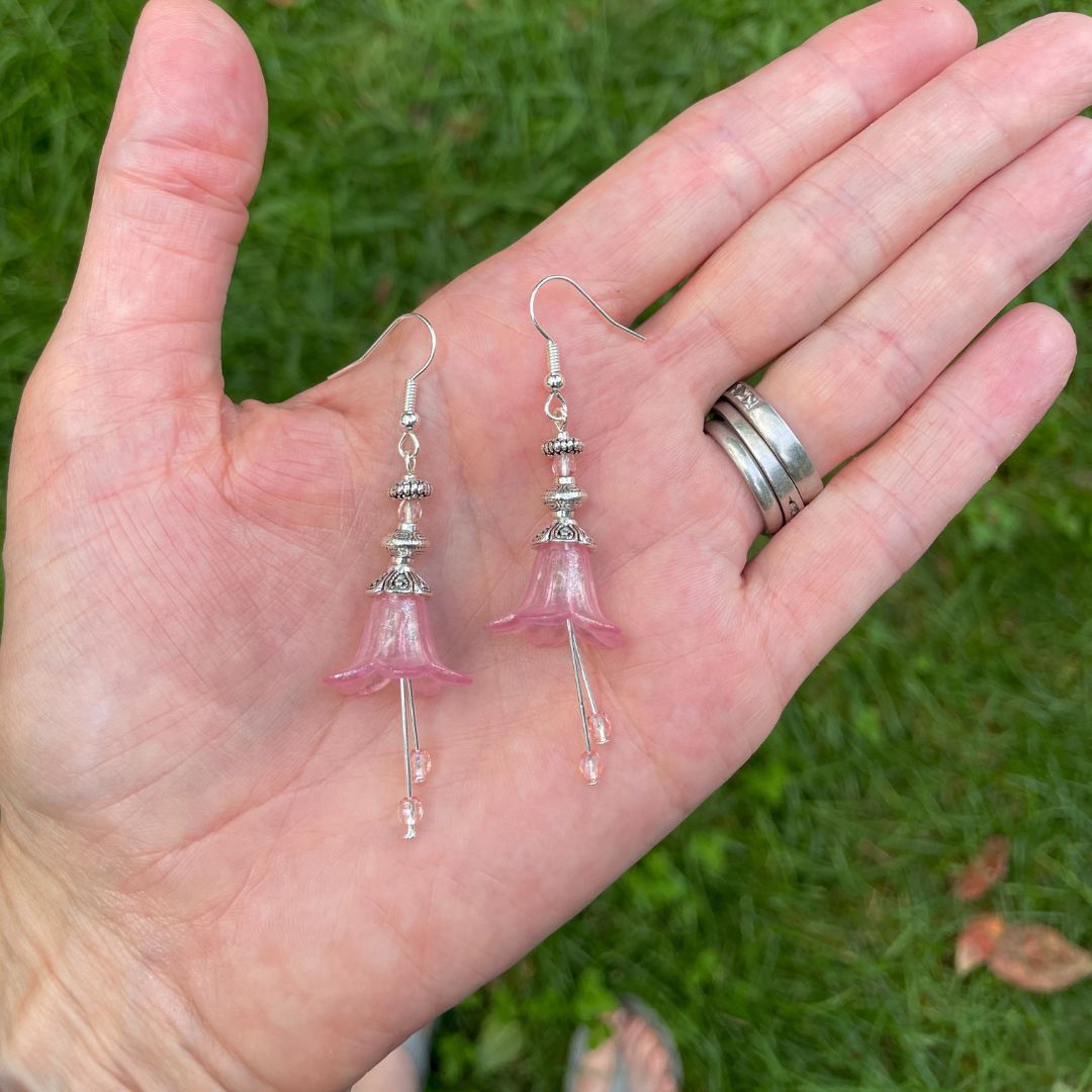 Pink Bell flower dangle earrings with pink stamen with silver finish. Earrings are held in a hand for size reference.