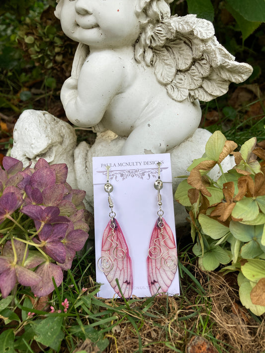 pink butterfly wing clip on earrings resting on an angel garden ornament with hydrangeas either side