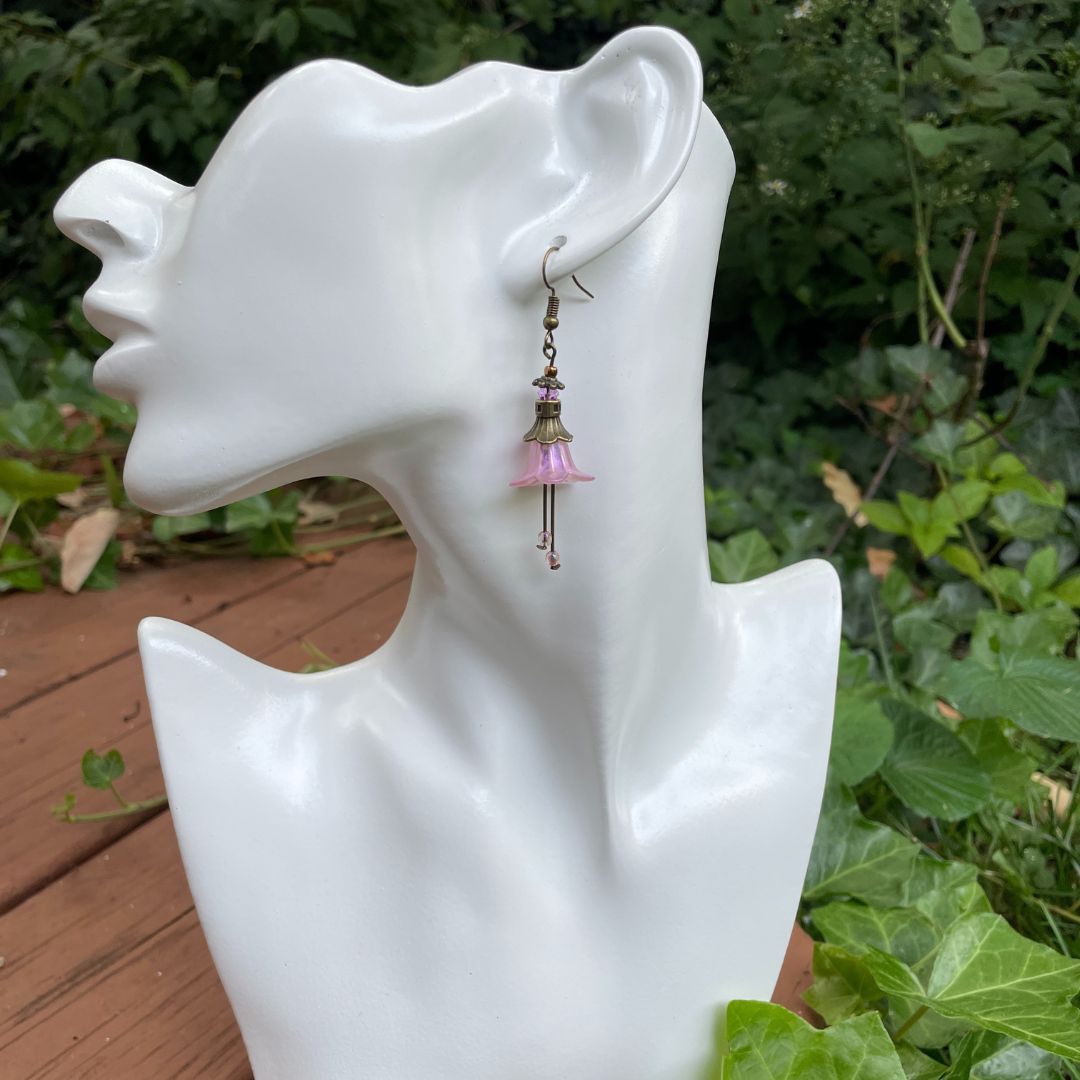 Pink Bell flower dangle earrings with purple crystal and pink crystal stamen with antique bronze finish. Earrings are displayed on a model.