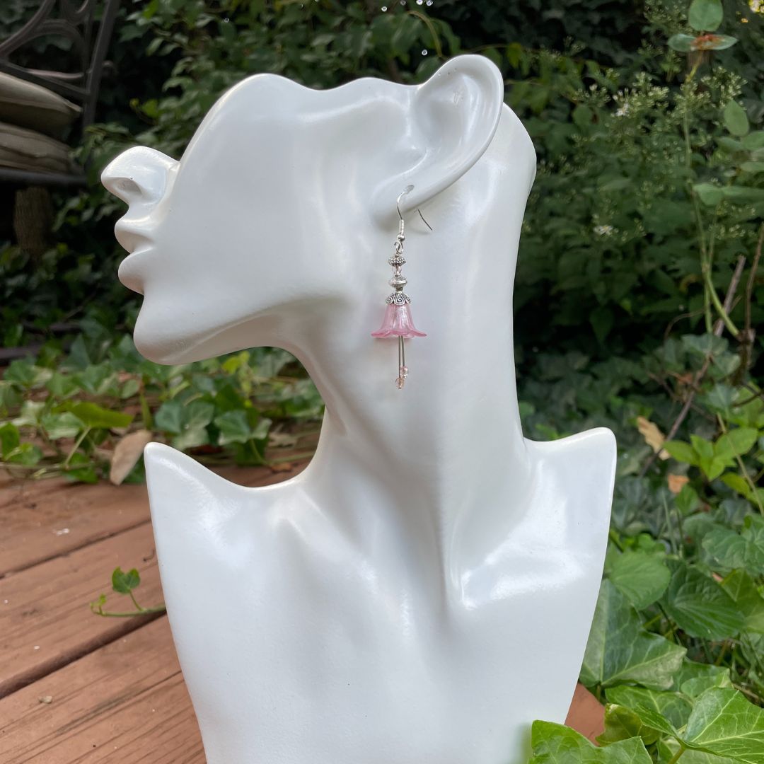 Pink Bell flower dangle earrings with pink crystal stamen with silver finish. Earrings are displayed on a model