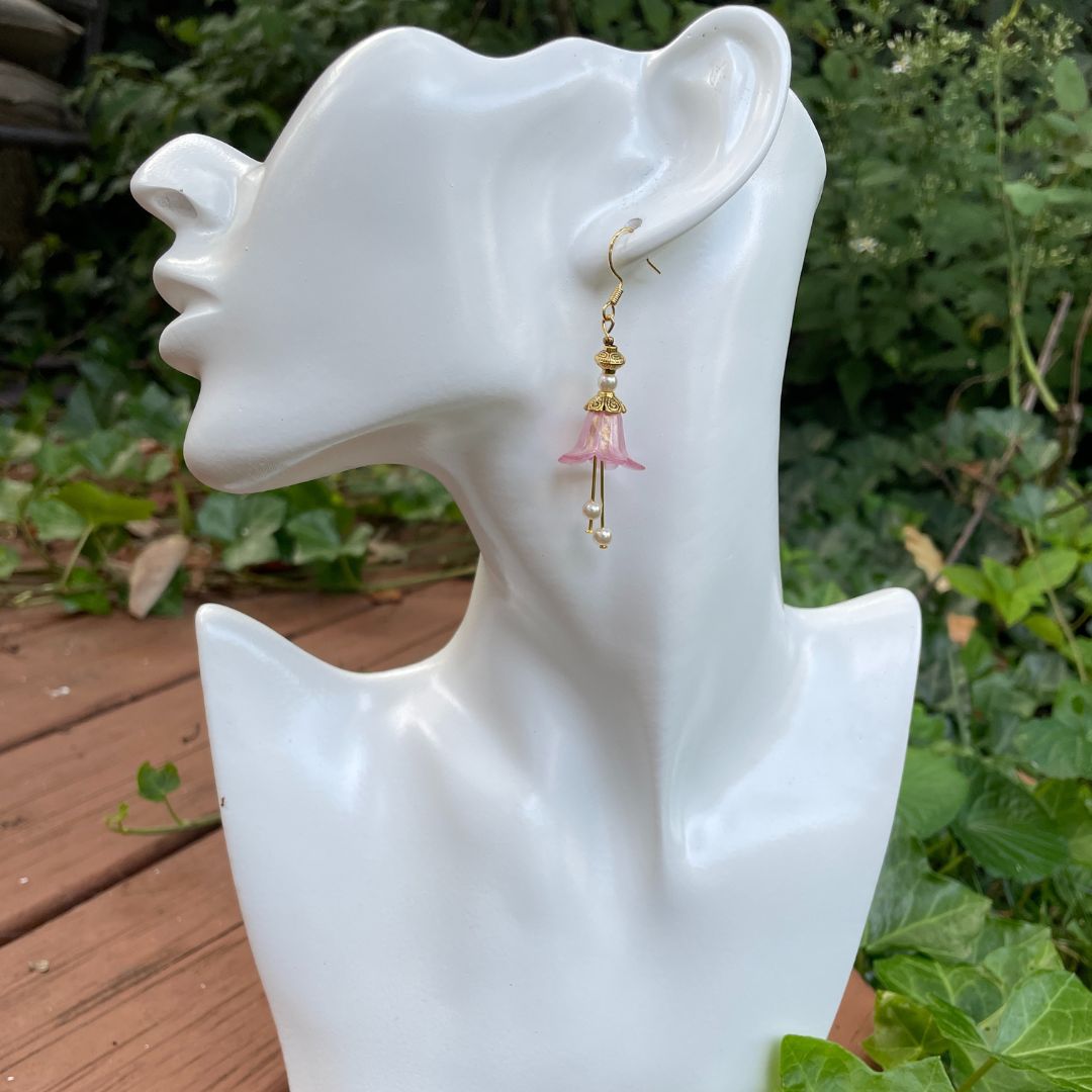Pink Bell flower dangle earrings with pearl stamen with gold finish. Earrings are hanging from a tree branch.