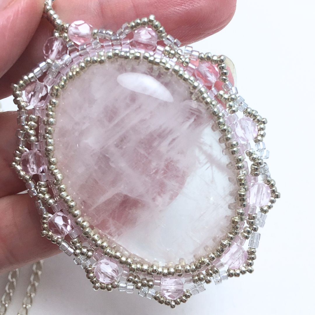 Close up of rose quartz beaded necklace held ina hand against a white background