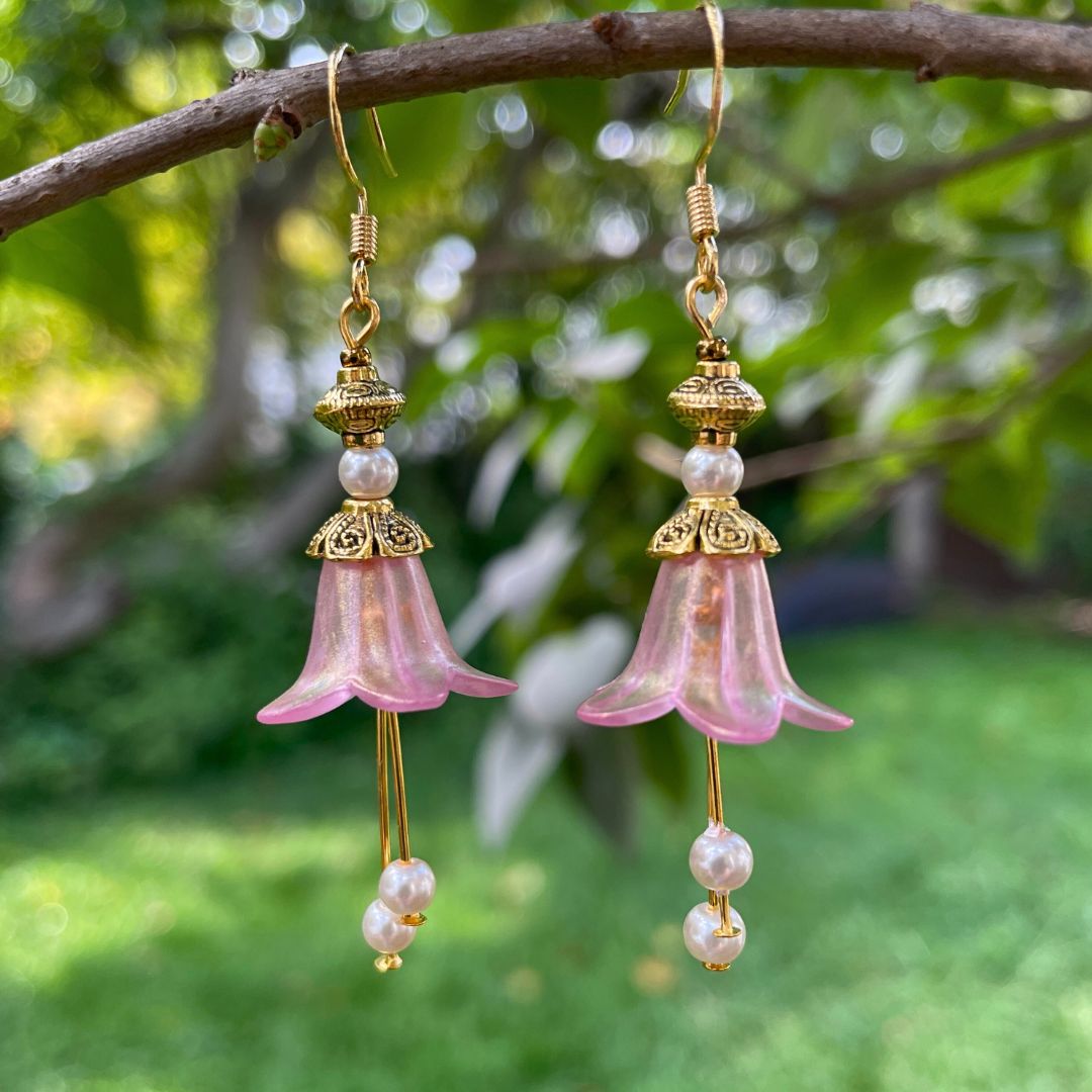 Pink Bell flower dangle earrings with purple crystal and pink crystal stamen with antique bronze finish. Earrings are hanging from a tree branch.