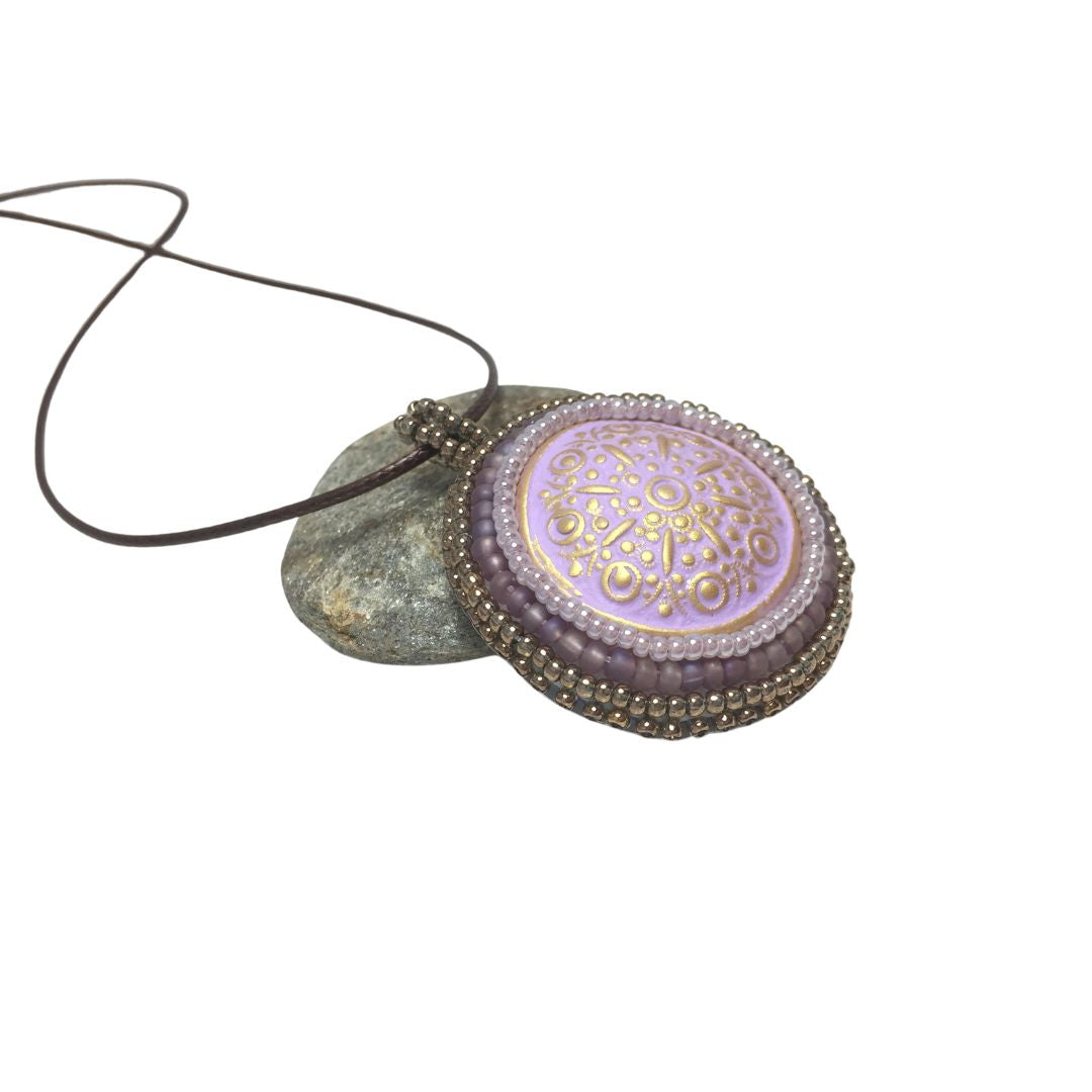 purple floral circle necklace resting on a rock against a white background.