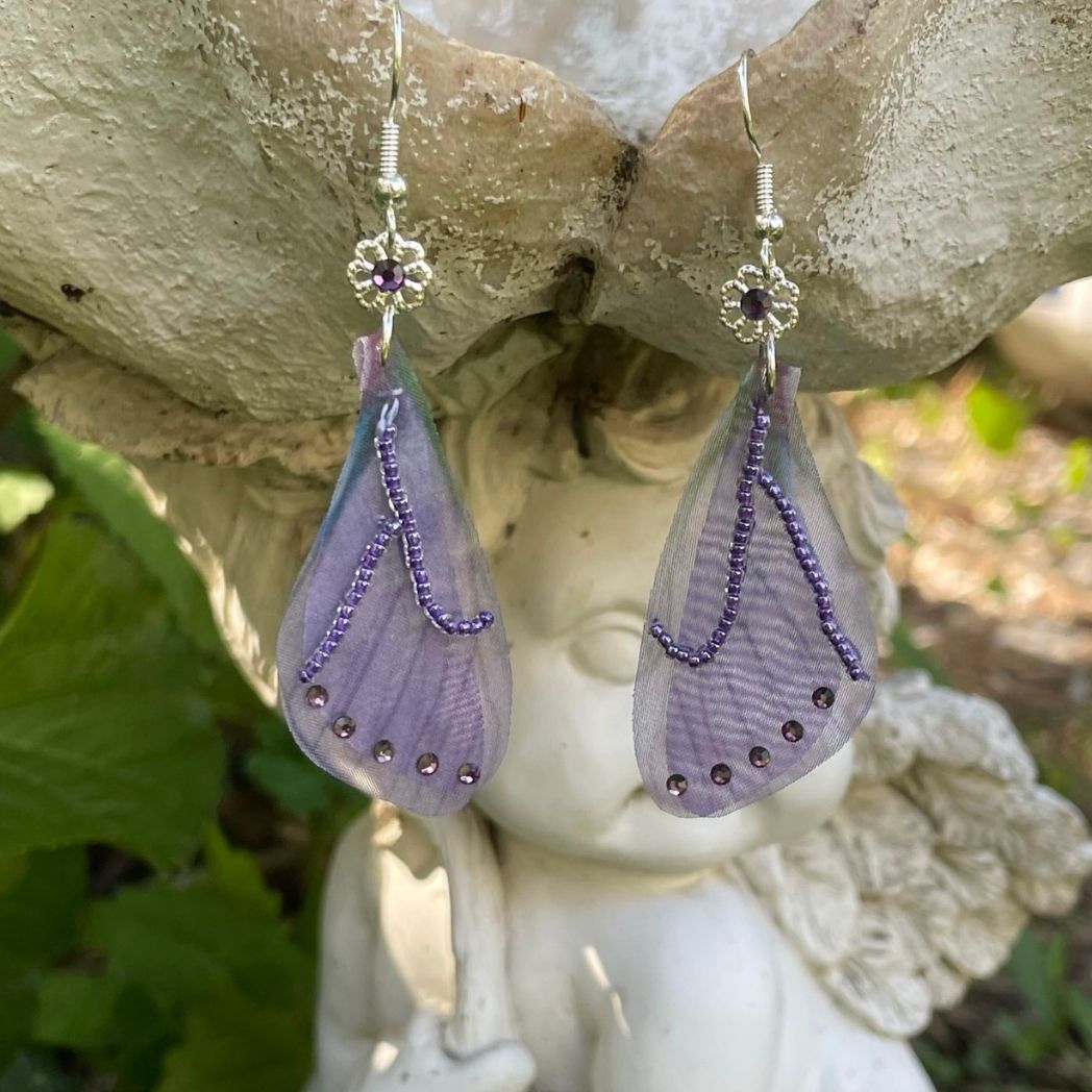 purple beaded fabric wing earrings with purple crystals and a flower bead with purple crystal above wings connecting to the ear wires