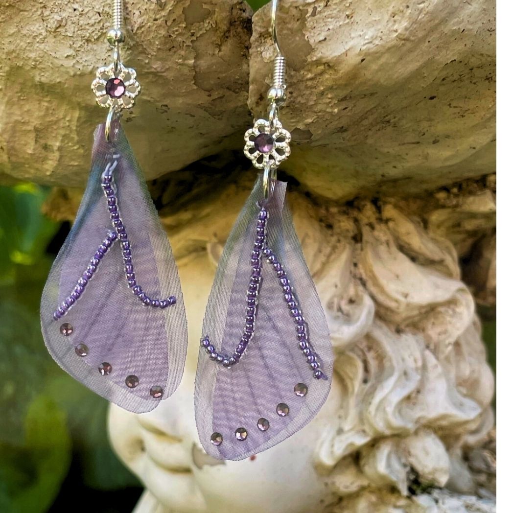purple beaded fabric wing earrings with purple crystals and a flower bead with purple crystal above wings connecting to the ear wires