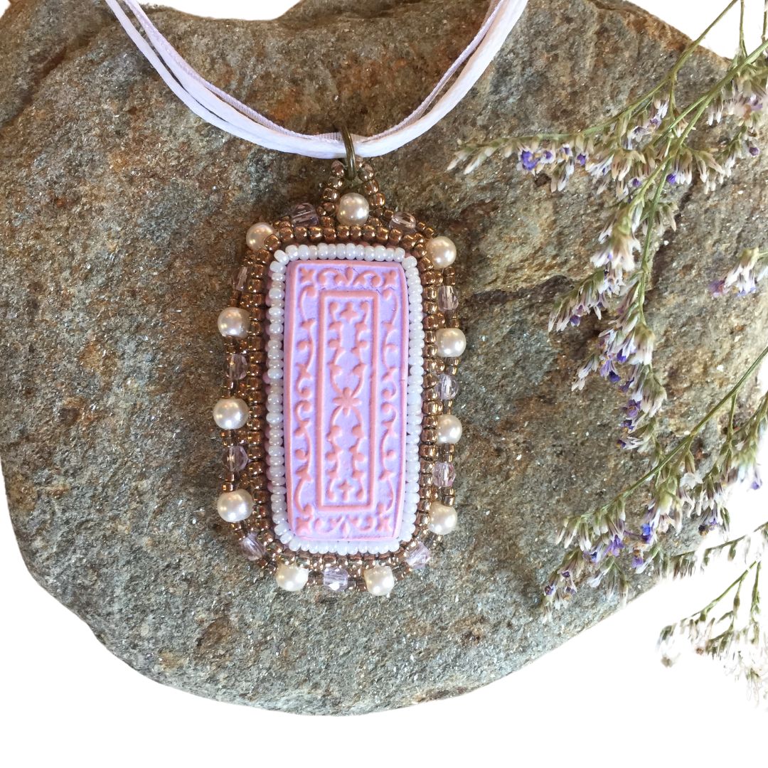 Purple beaded floral necklace laying flat on a rock with floral arrangement to the right side.