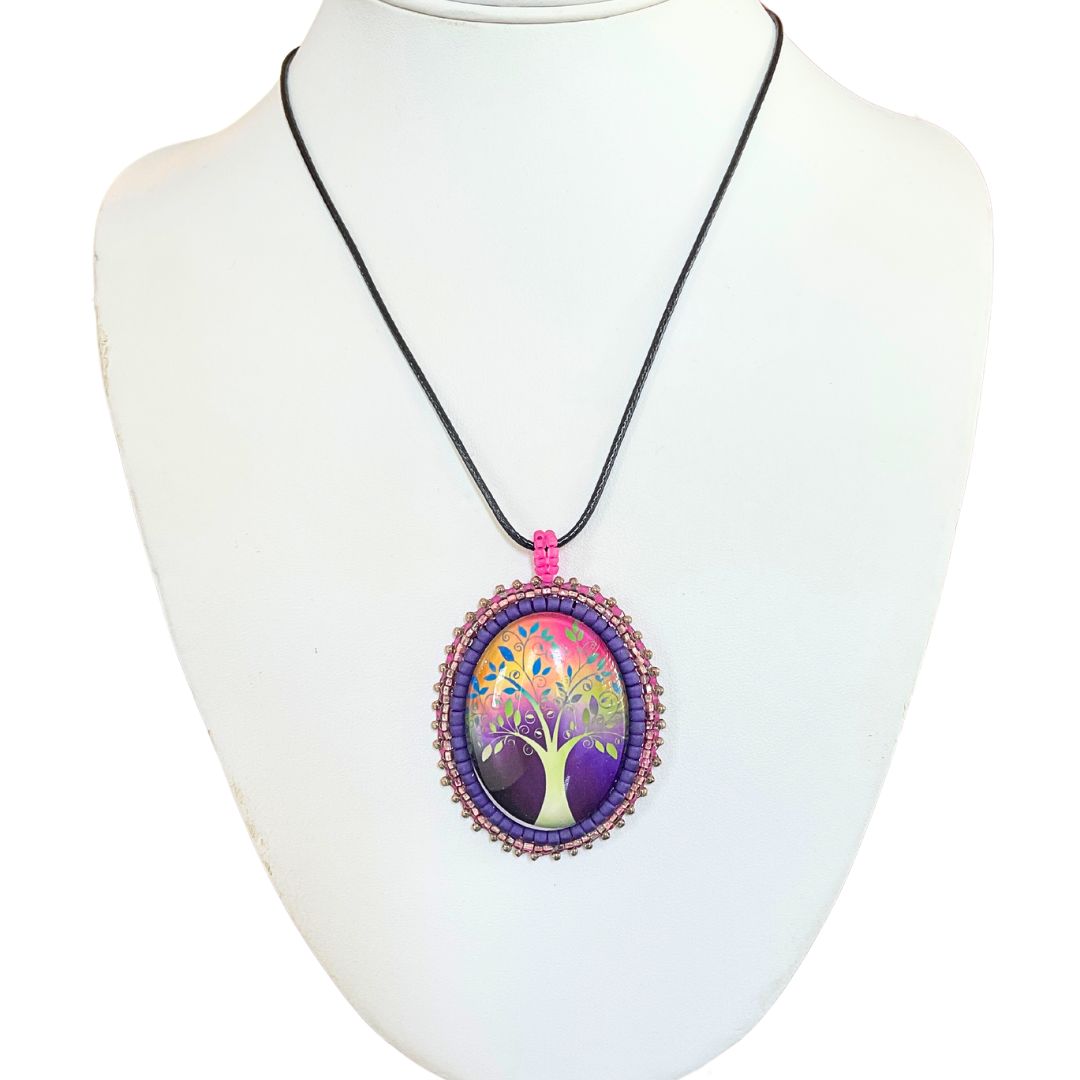 Oval pendant with whimsical tree with purple, red and pink background with pink and purple glass seed bead edging on a black cord necklace.