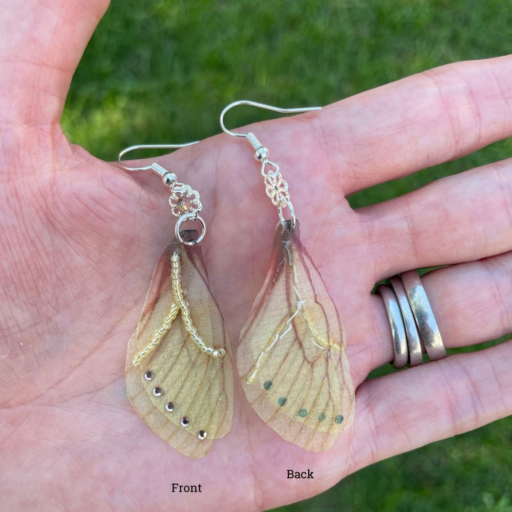 Yellow sheer fabric beaded butterfly wing earrings with peach color crystals and a flower bead connect the wings to the ear wires. Held in a hand