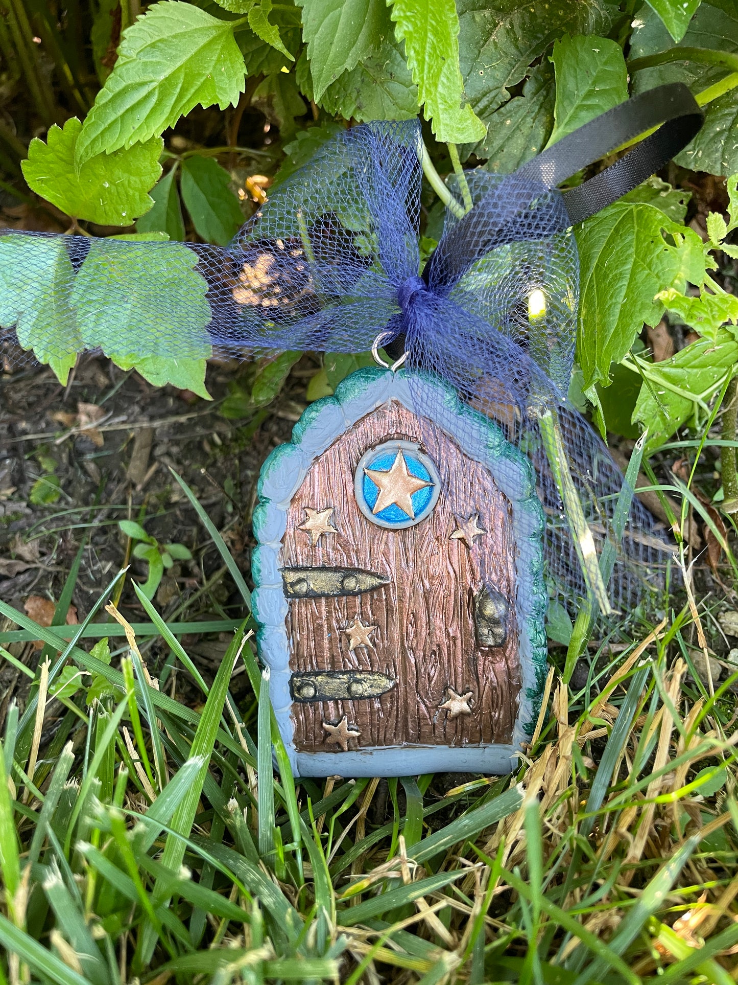 star fairy door with blue tulle bow nestled amongst greenery