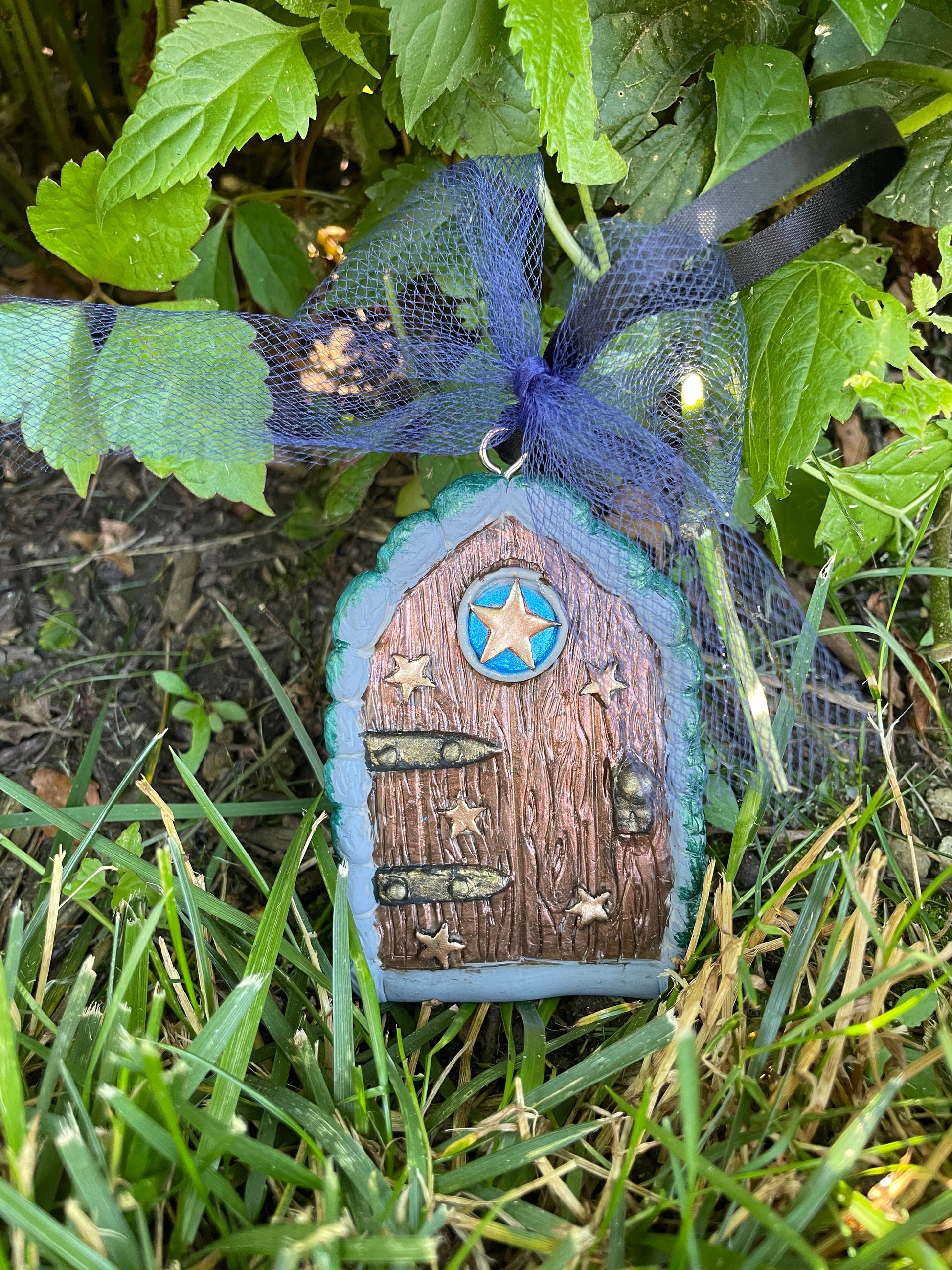 star fairy door with blue tulle bow nestled amongst greenery