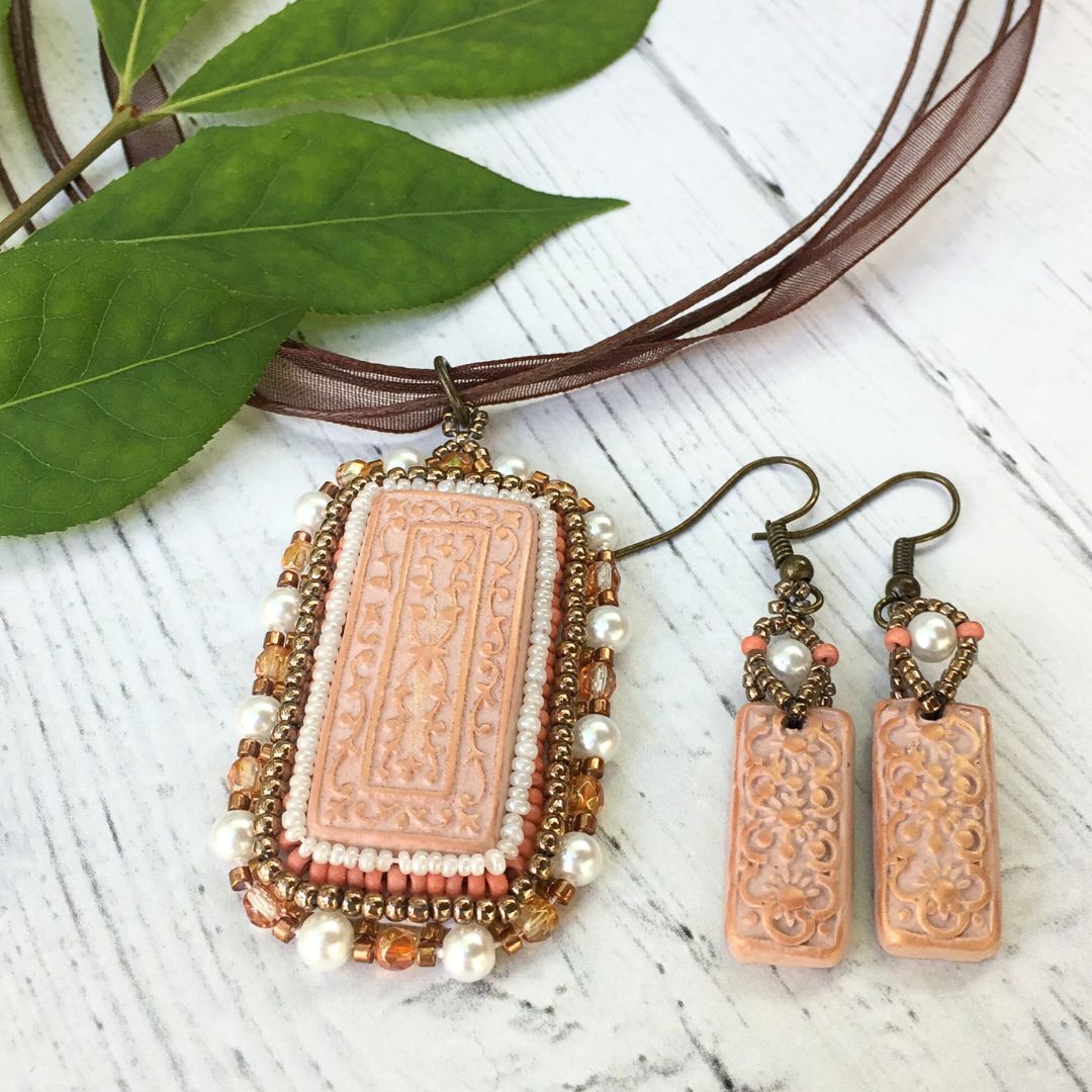Beige floral beaded necklace jewelry set laying flat on a white wood surface with greenery in background.