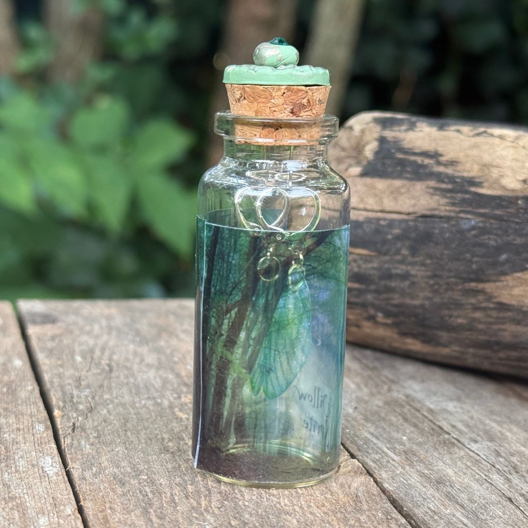Small glass bottle with cork lid containing a green butterfly on a wooden surface with a blurred natural background