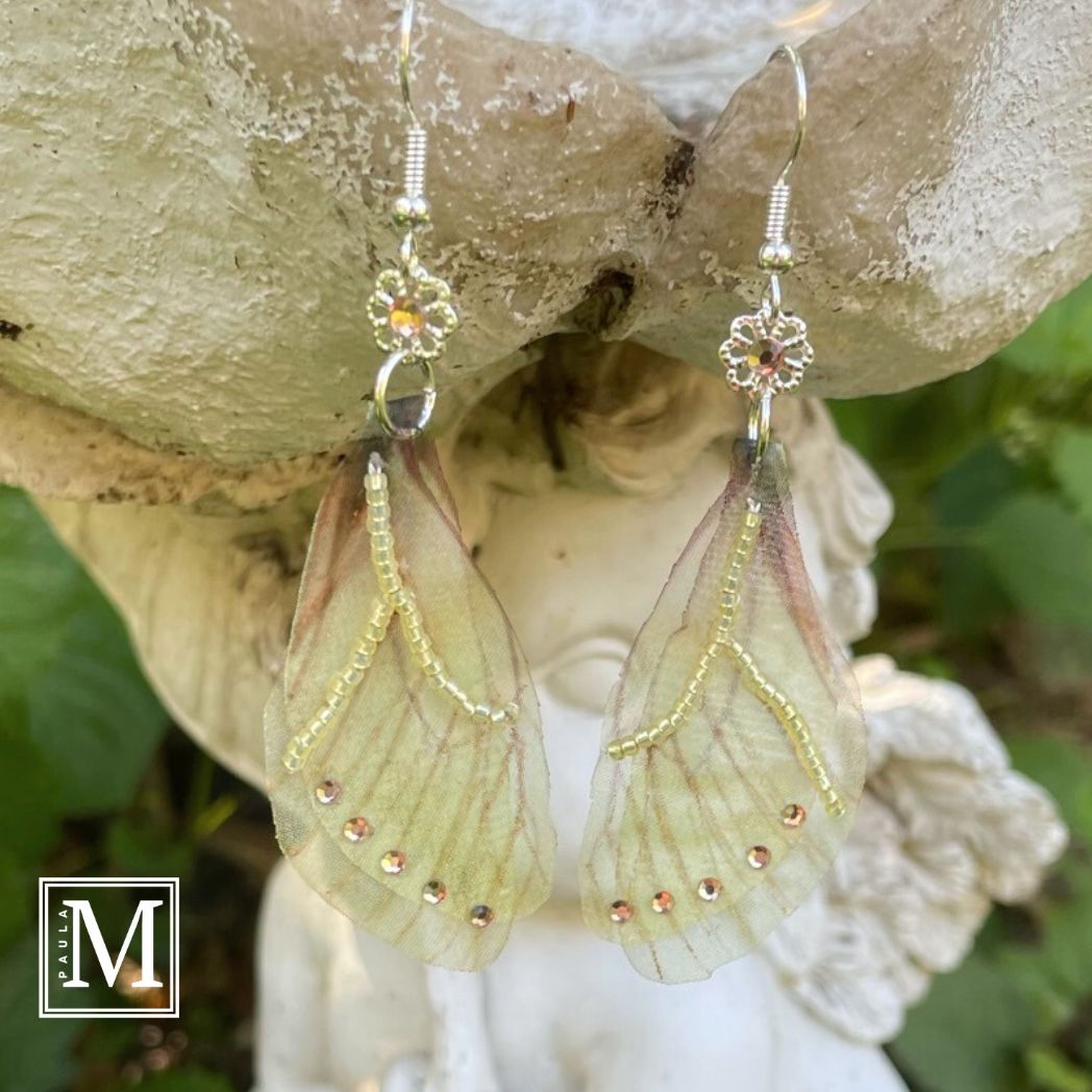 Yellow sheer fabric beaded butterfly wing earrings with peach color crystals and a flower bead connect the wings to the ear wires. Hanging from a garden ornament.
