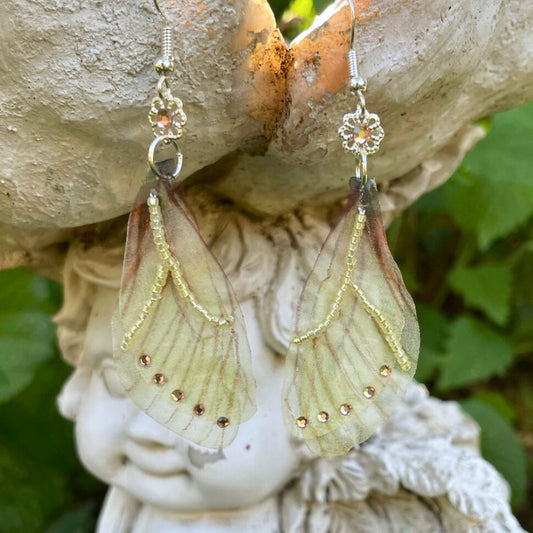 Yellow sheer fabric beaded butterfly wing earrings with peach color crystals and a flower bead connect the wings to the ear wires. Hanging from a garden ornament.