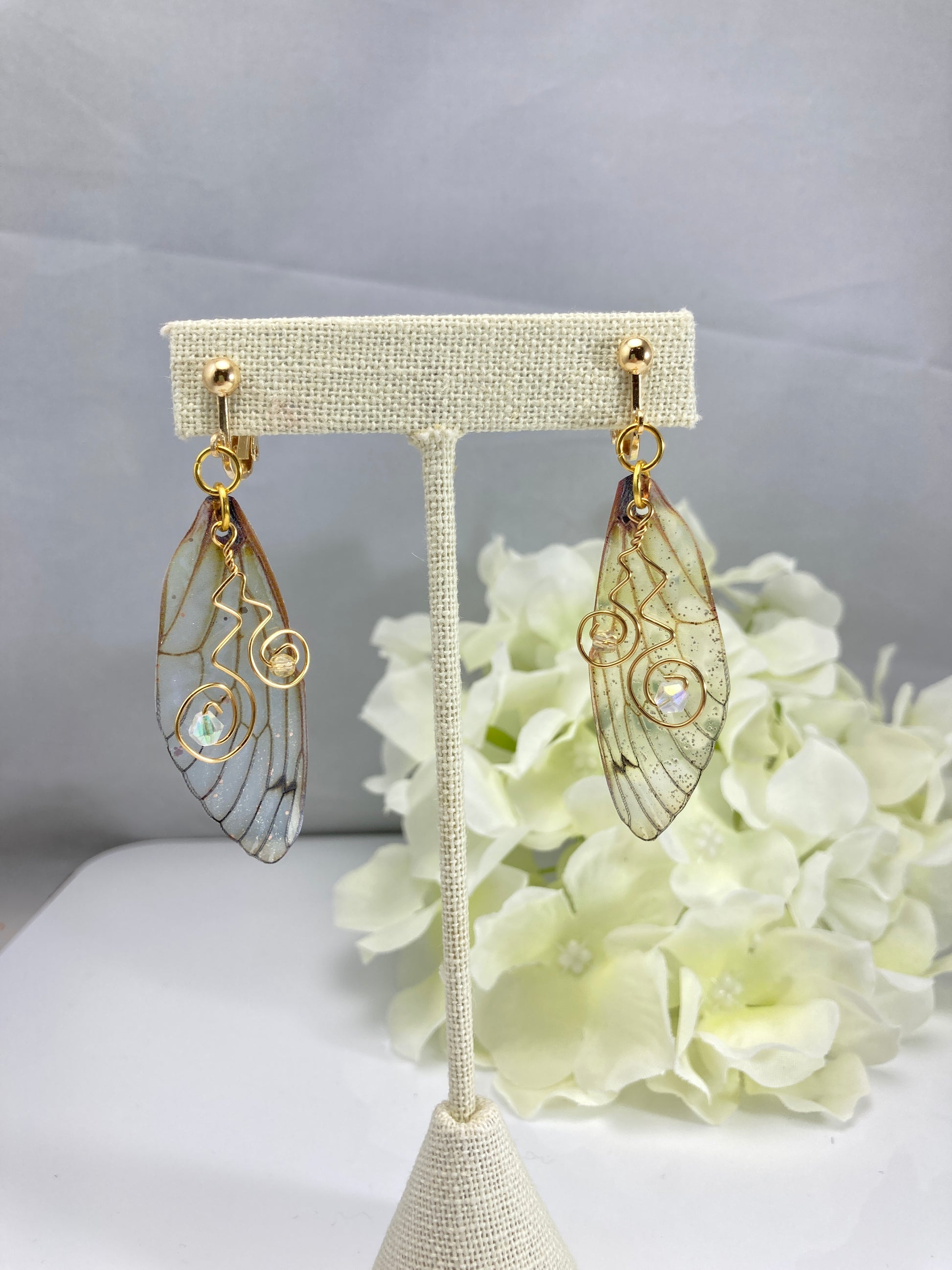 yellow butterfly wing clip on earrings  dangling from an earring display with a yellow flower in the background
