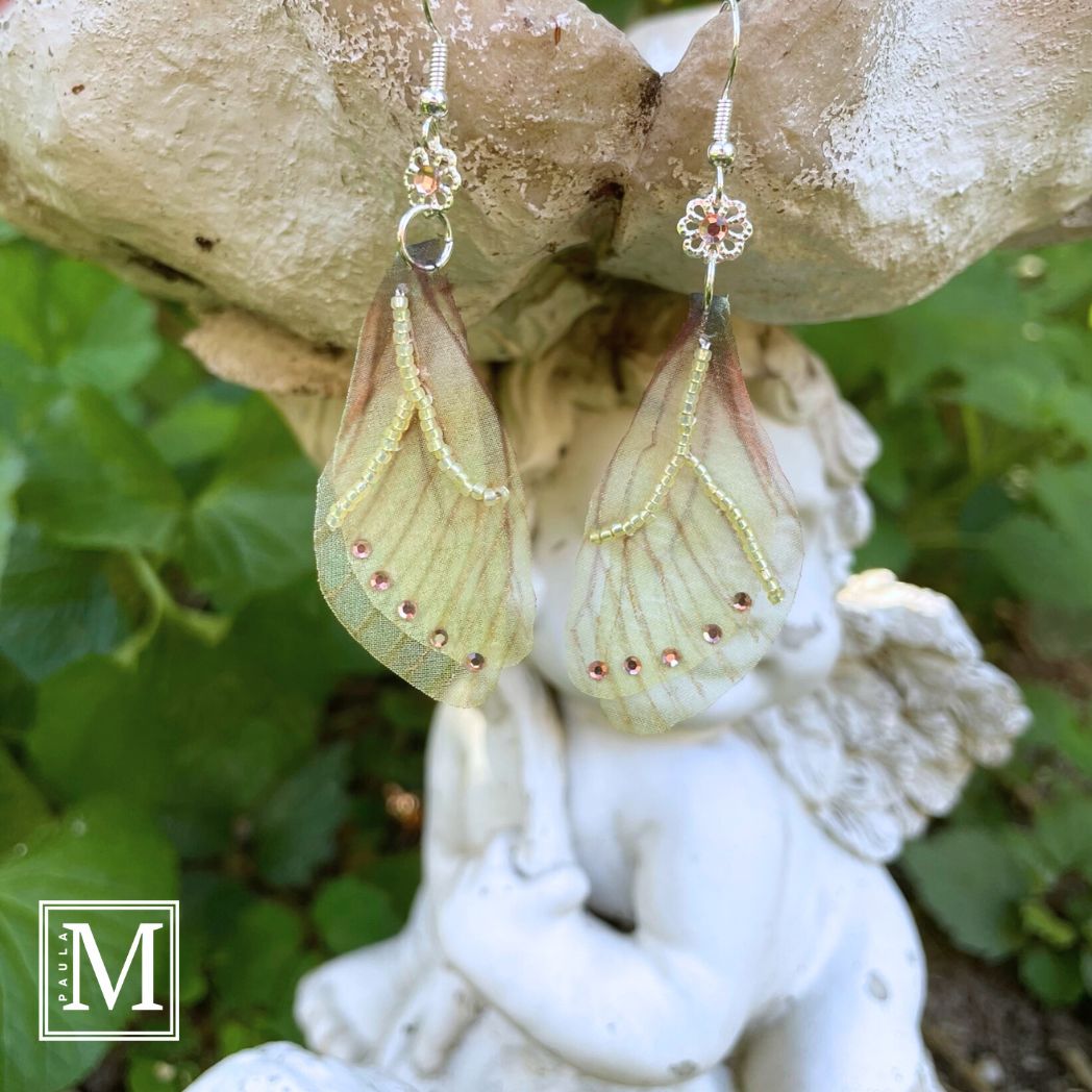 Yellow sheer fabric beaded butterfly wing earrings with peach color crystals and a flower bead connect the wings to the ear wires. Hanging from a garden ornament.