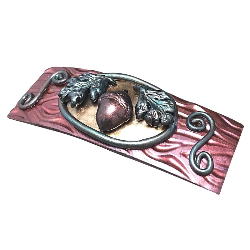 Side profile of an Autumn hair clip with acorn and oak leaves and swirls on a russet pink textured base.