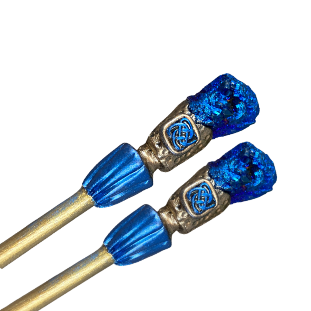 Two wood hair sticks with metallic blue druzy crystal at one end and polymer clay Celtic knot detail in gold and blue clay.