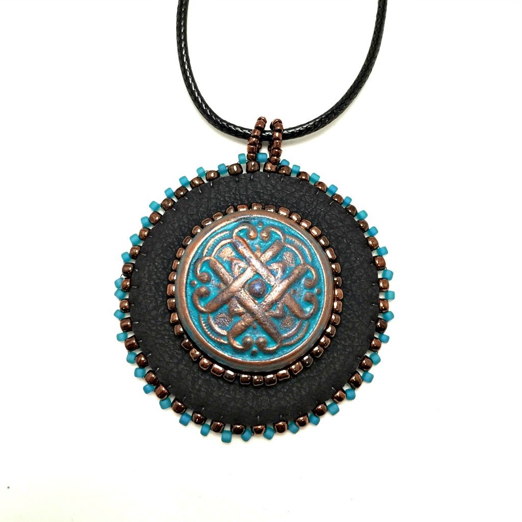 Black faux leather round pendant with beaded edge in gold and turquoise with a patina Celtic knot motif in the center with beading. Necklace is on a black cord chain.