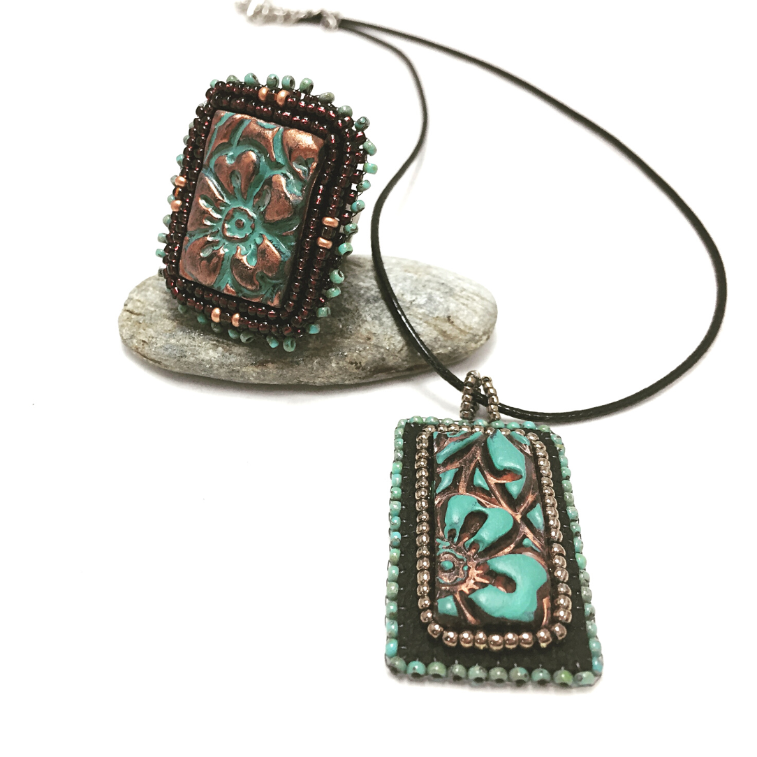 A rectangle Patina Flower beaded Necklace and Ring Set. Necklace is resting on a pebble.