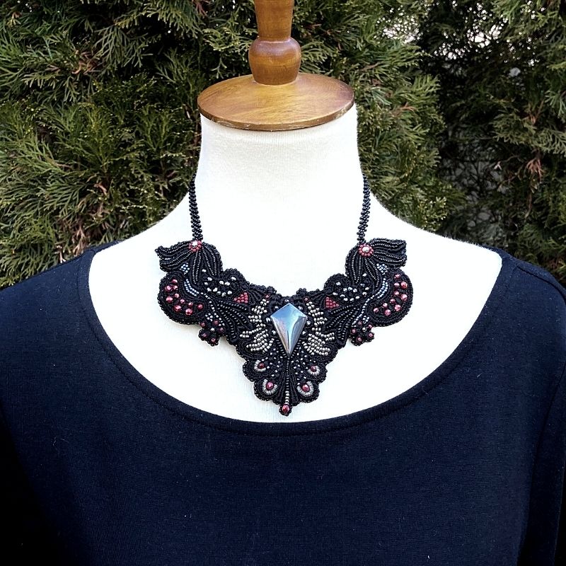 Large gothic beaded collar necklace with hematite beads display on a model with a black dress outside with a fir tree in the background