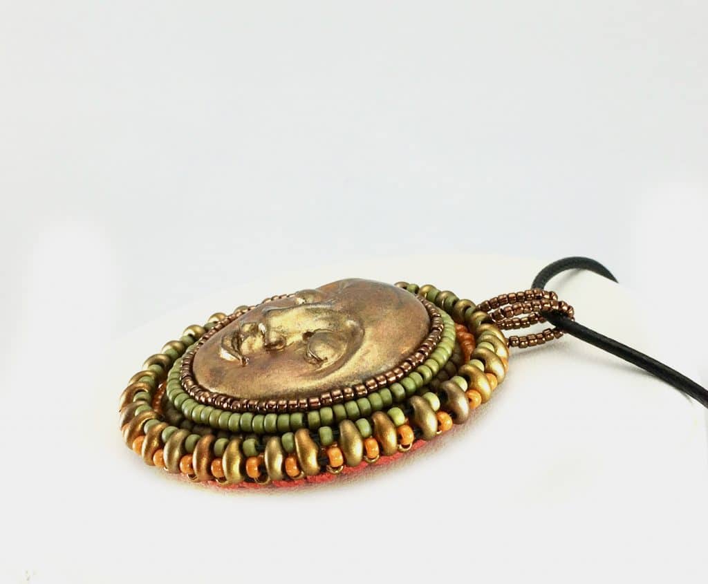 Side profile of sun face round pendant in gold with green, gold and orange beaded edging.