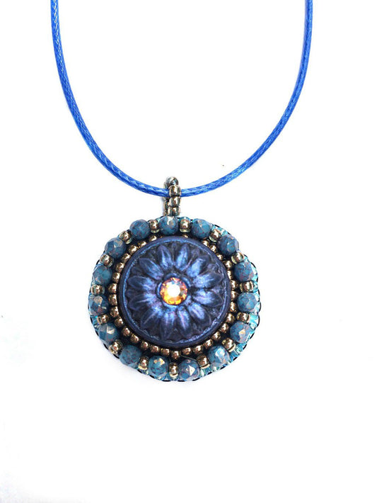Blue daisy handpainted clay pendant with yellow center crystal with blue and gold crystal beading around the edges and a blue cord necklace chain.