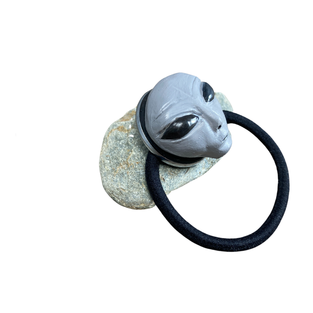 Side profile view of a gray alien head hair tie resting on a rock