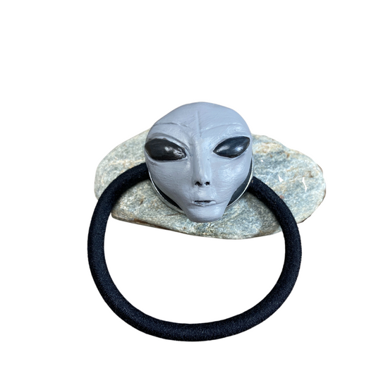 Gray Alien head hair tie resting on a rock.