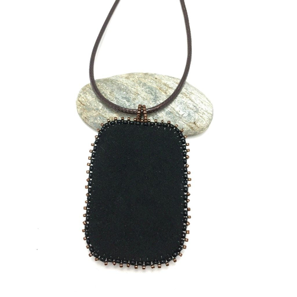 Back of large copper patina textured floral Rectangle pendant with turquoise and bronze beaded edging on a brown cord necklace chain.