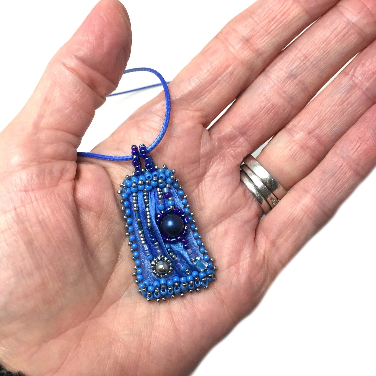 Beaded blue shibori silk necklace held, and hand for size reference.