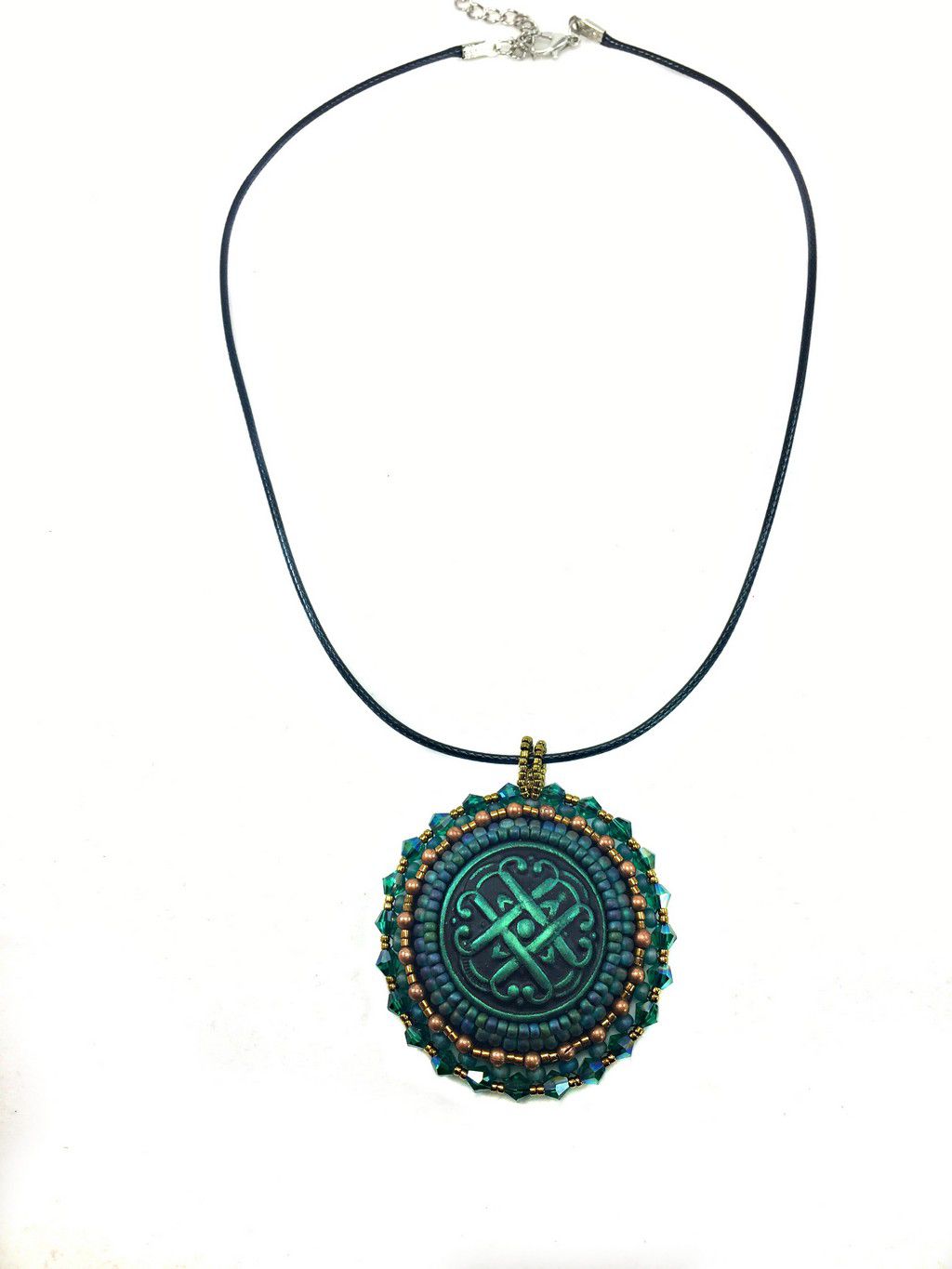 A green Celtic love knot motif, surrounded by green and gold seed bead edging  and green  crystals. Pendant is on a black cord chain.