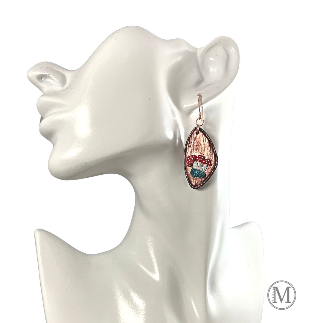 Geometric shaped bronze clay dangle earring with small clusters of Amanita mushrooms on a model.