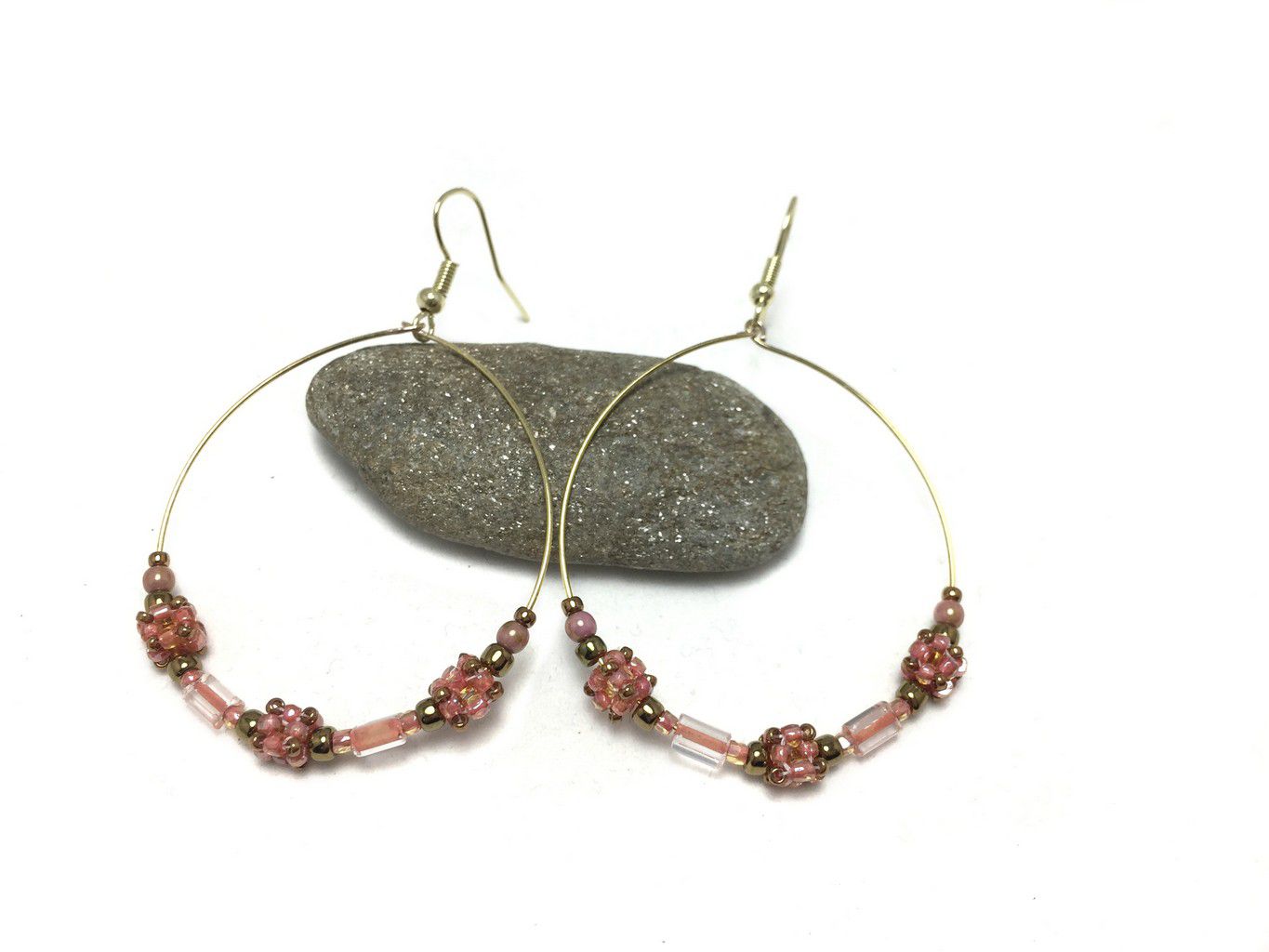 2 inch gold wire hoop earrings with coral cube beads, crystals and gold beads. Earrings are resting on a pebble.