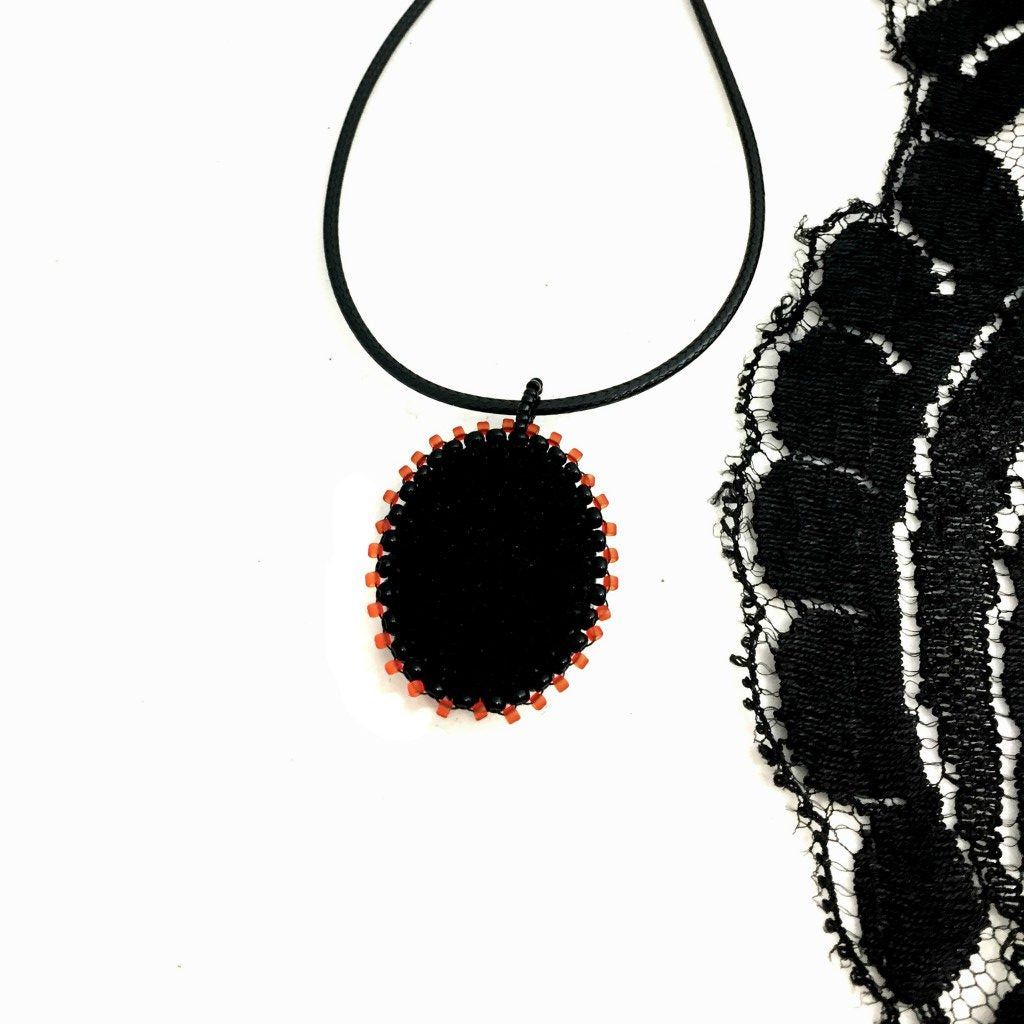 Back of Oval red and black beaded pendant necklace. A piece of black lace is to the right hand side of the photo.