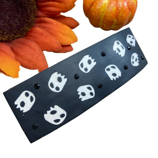 Black polymer clay hair barrette with cute white ghosts and black crystals. An orange sunflower and pumpkin are in the background.