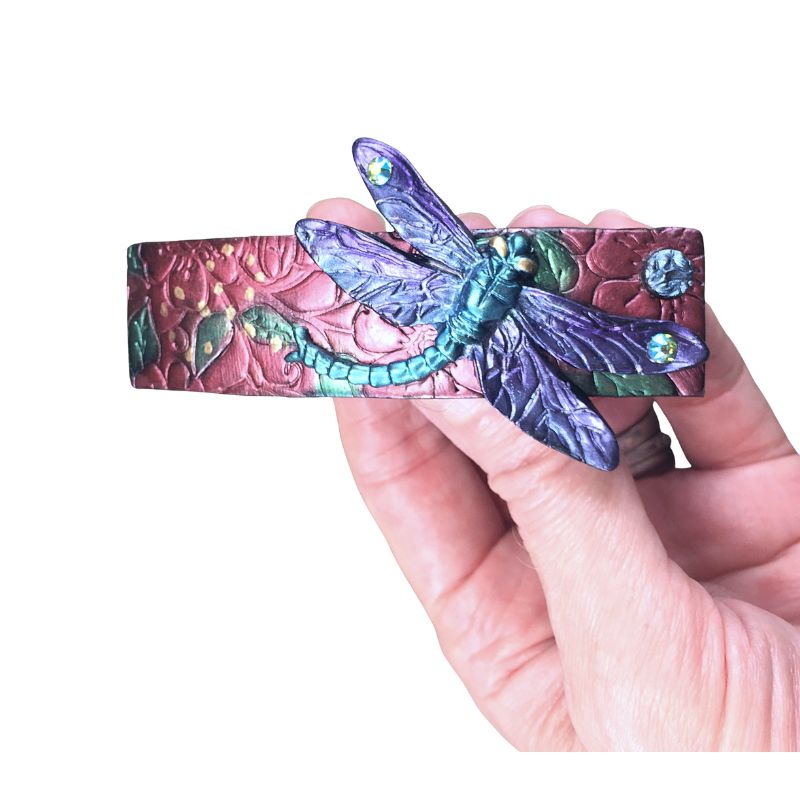 Dragonfly polymer clay hair barrette with pink base and purple and green dragonfly held in a hand.