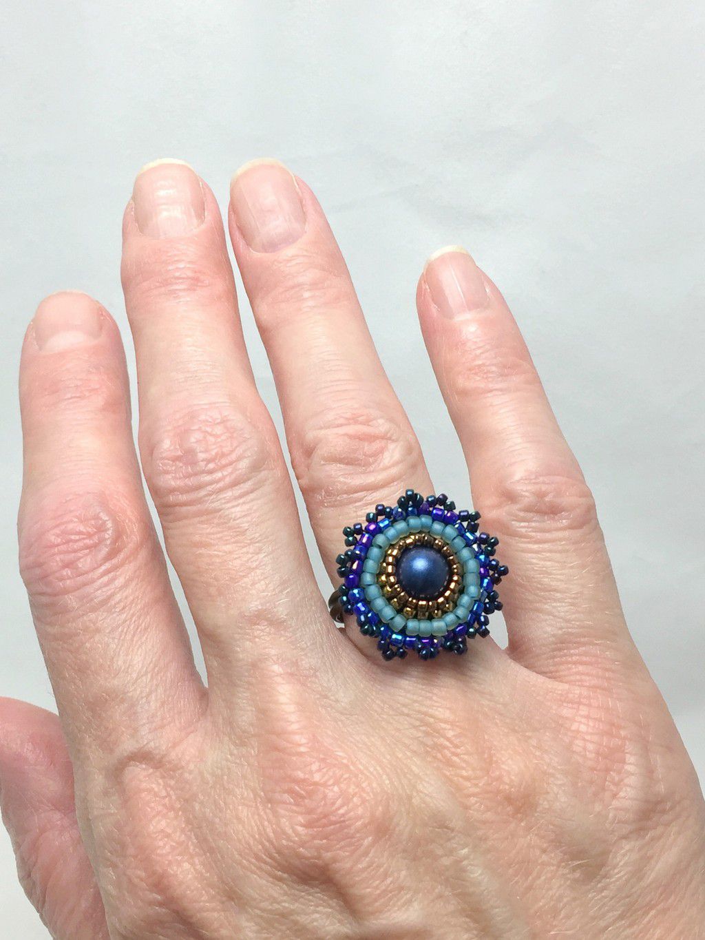 Model wearing beaded mandala ring in turquoise and green.