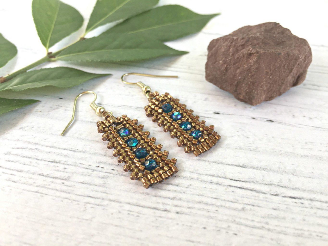 Blue Zircon crystal lace rectangle earrings laying flat on whitewash wood surface with a leaf and rock