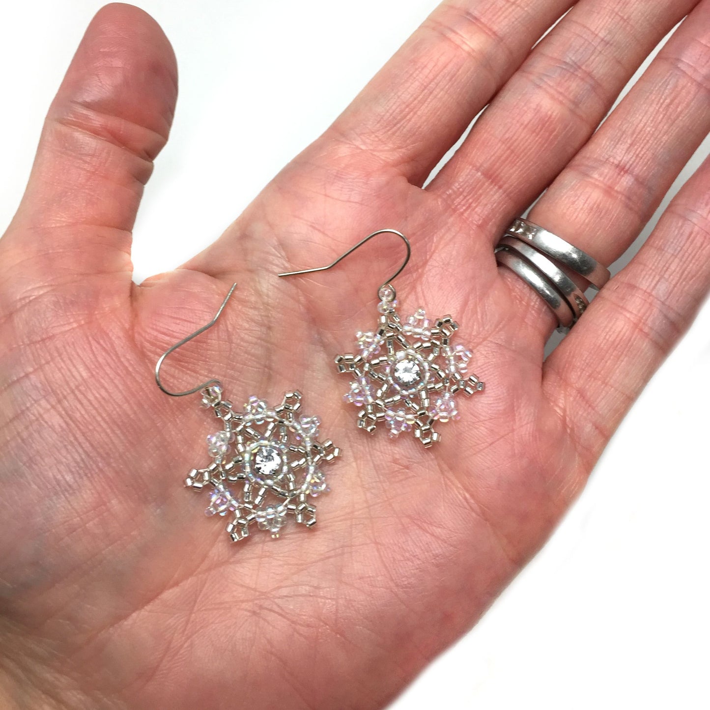 Large silver and blue snowflake earrings held in a hand for size reference