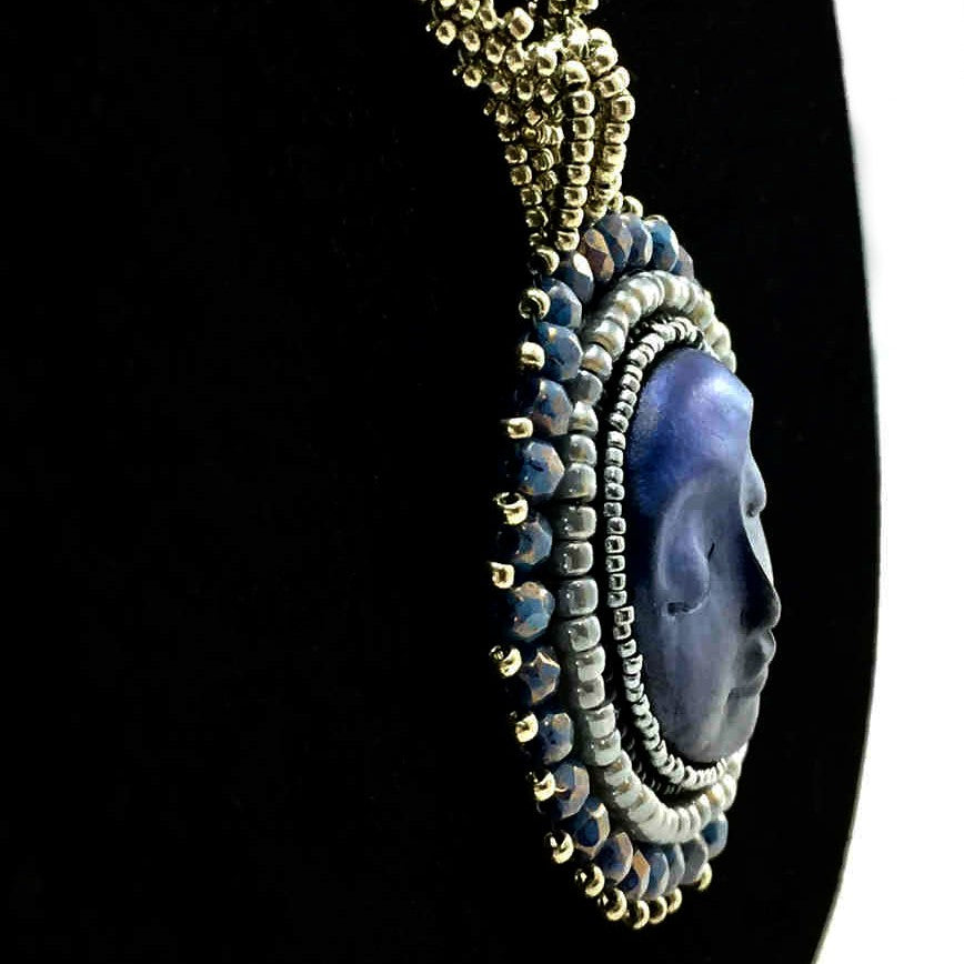 Side profile of A necklace with a blue moon face surrounded by silver and blue beadwork on a long silver seed bead chain with blue crystals and ball and loop closure