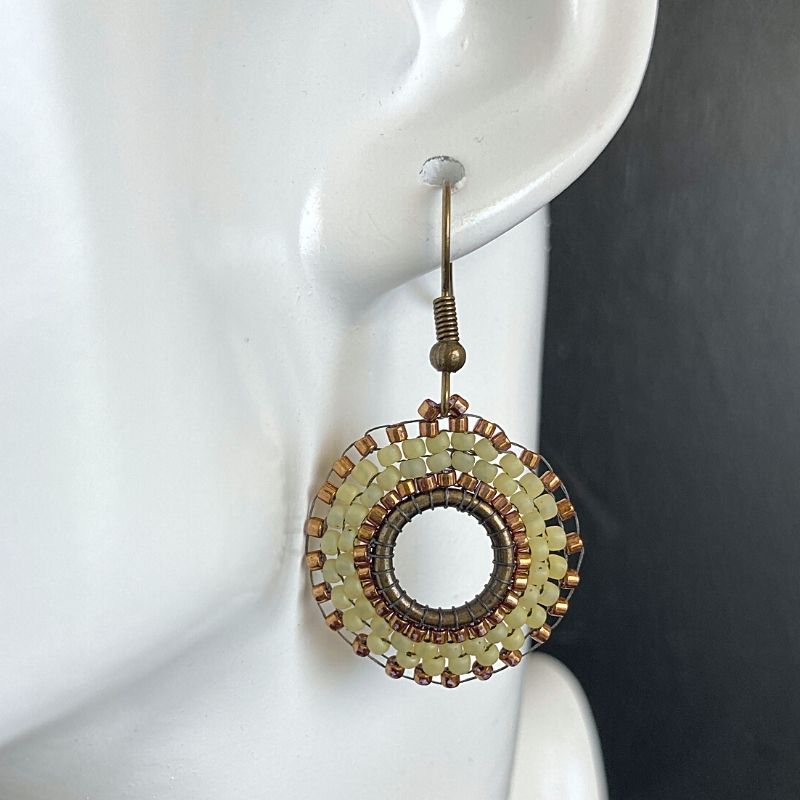 Sage green and gold seed bead earrings on a model.