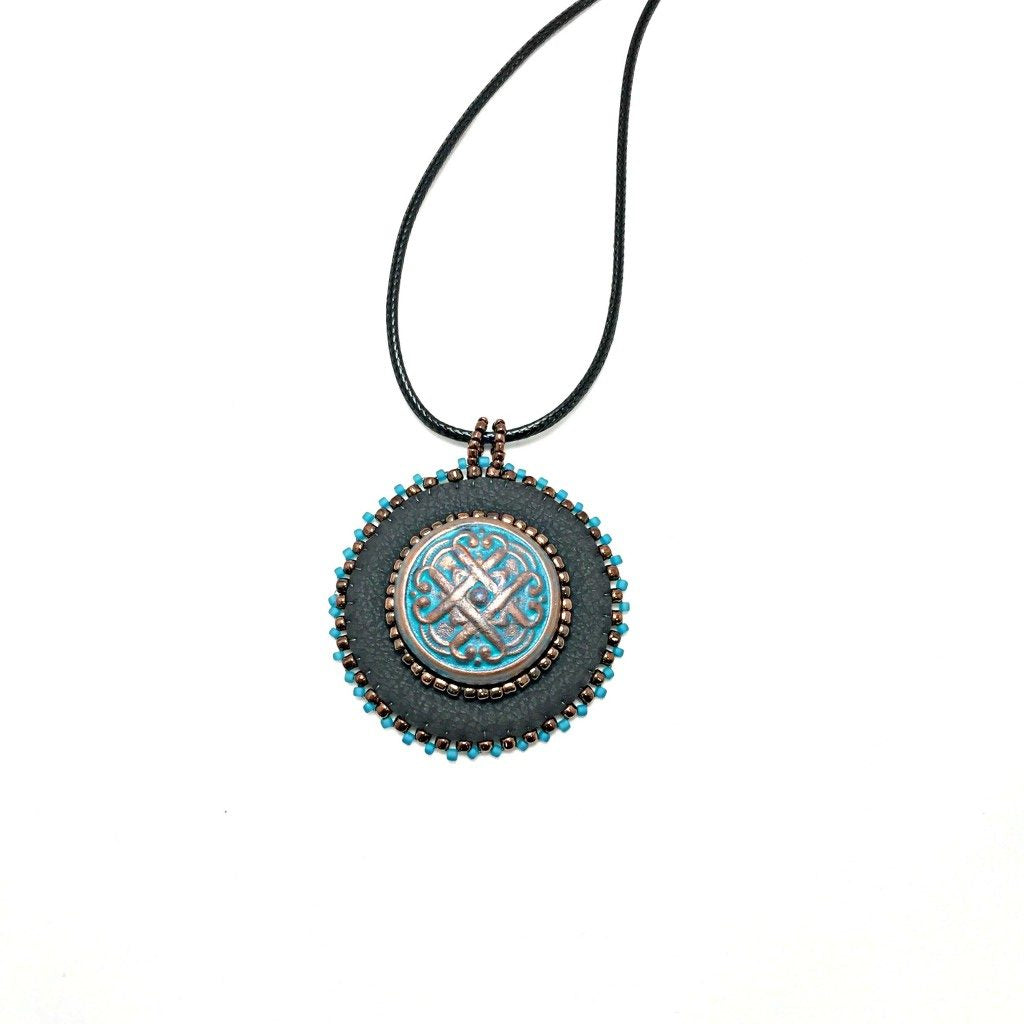 Black faux leather round pendant with beaded edge in gold and turquoise with a patina Celtic knot motif in the center with beading. Necklace is on a black cord chain.
