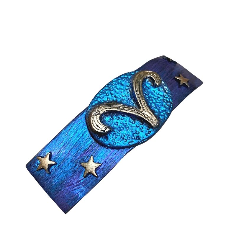 Side view of blue and purple hair clip with a gold Aries symbol in the center with 2 gold stars on each side.